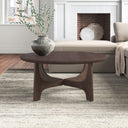 Skyler round walnut brown wood coffee table with cross arched pedestal base styled in a living room