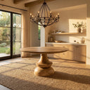 Musa Round Dining Table in a natural wood finish styled in a warm, sunlit dining room with a modern chandelier.