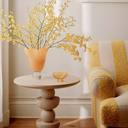 Mylo round wood side table styled next to a yellow striped boucle armchair with floral vase