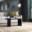 Lee oval black wood coffee table in a moody living room styled with a large round mirror and colorful vintage rug