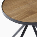 Close-up of the Cayden Side Table showing the wood-grain surface, curved black tabletop border, and angled black legs beneath.
