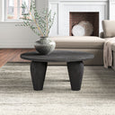 Alberto round black wood coffee table with thick tapered tripod legs in a modern living room