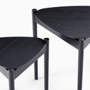Detailed close-up of Lewis Tripod Nesting Side Tables highlighting the curved tabletop edges, black wood grain, and tripod-style leg construction.