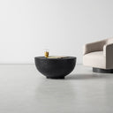 Finnley round black wood drum coffee table with textured bowl base styled in a room