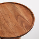Jaime Tall End Table - round wooden side table with a raised-edge tabletop and sculptural pedestal base beside a lounge chair.