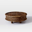 Chandler round carved wood coffee table three-quarter studio view showcasing lattice fretwork apron base