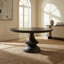 Dark wood Musa Round Dining Table positioned on a textured rug beneath an arched window in a sophisticated dining space.