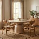 Tomas Round 6 Seater Dining Table styled in a warm dining room, featuring a light wood round tabletop, sculptural pedestal base, and six wooden dining chairs.